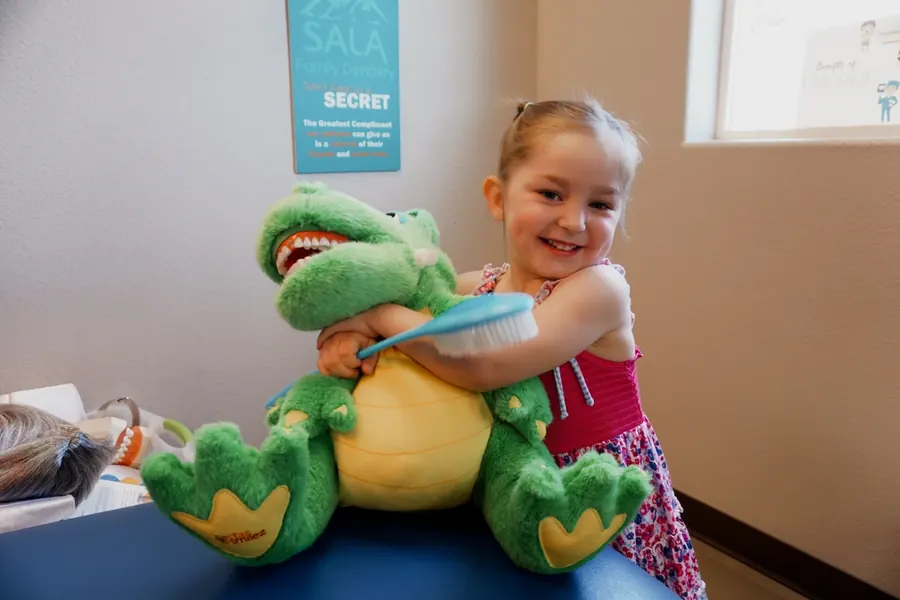 A young patient hugging a toy dinosaur and its toothbrush.