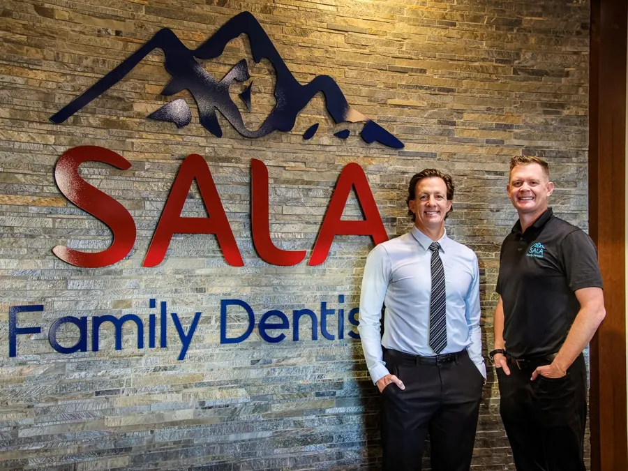 Dr. Jason Sala and Dr. Todd Sala beside the SALA Family Dentistry sign in the practice.