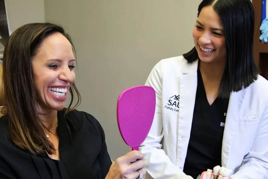 A patient checking her smile in a hand mirror with her dentist.